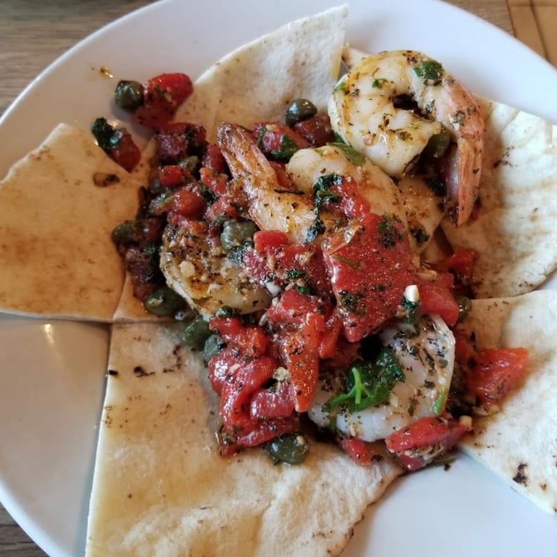 Dalia's Mediterranean shrimp dish with red peppers, capers, and herbs on pita bread.